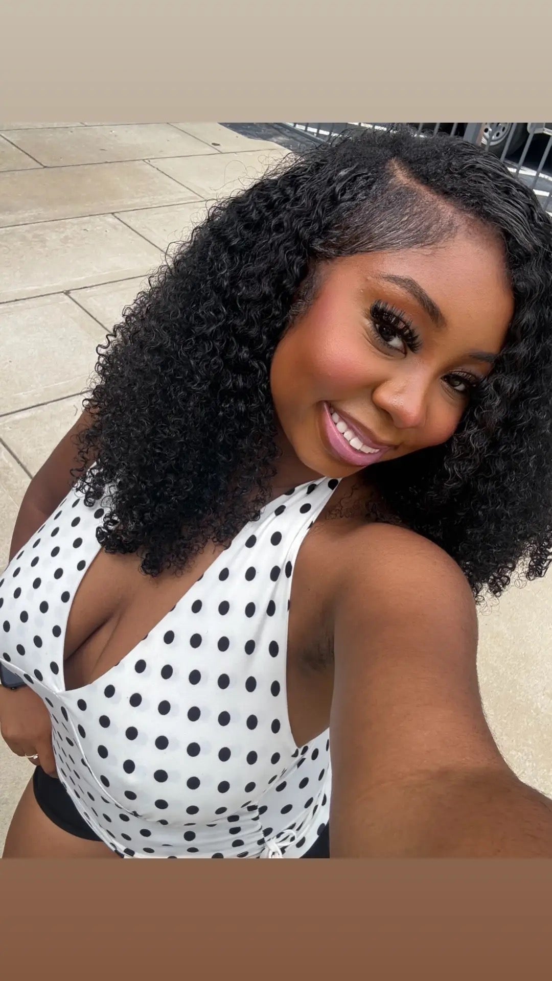 Woman in a polka dot swimsuit with curly hair, sitting on a tiled floor.