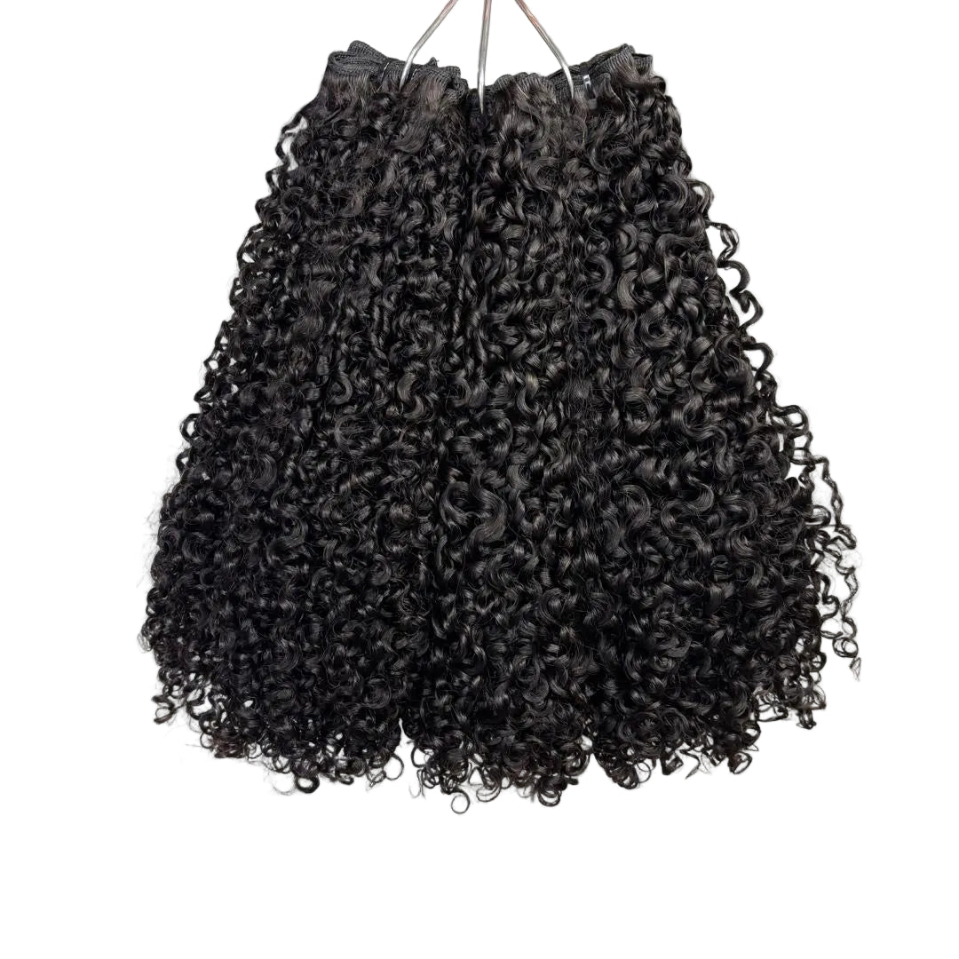 Black curly hair extensions on a white surface with a plant in the background