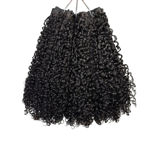 Black curly hair extensions on a white surface with a plant in the background