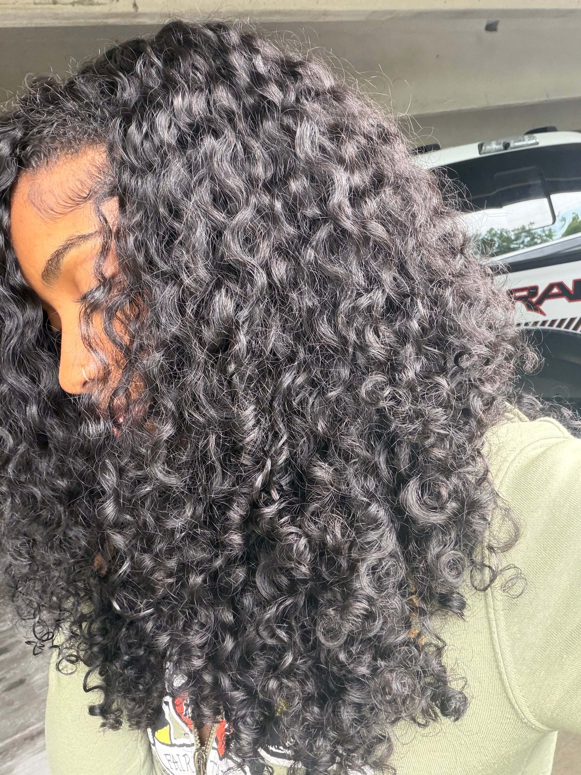 girl with burmese curly bundles wearing a green jacket outdoors.