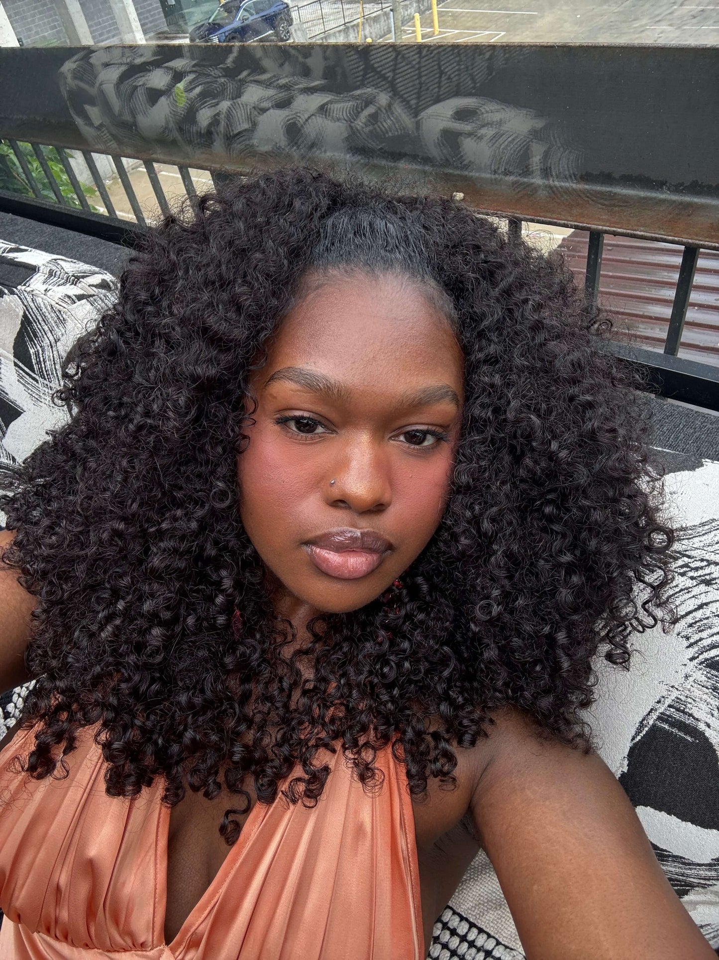 Woman with pixie curly bundles wearing an orange top on a balcony
