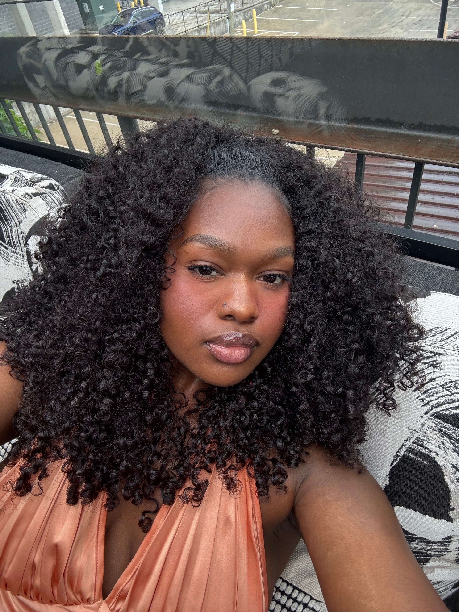 Woman with pixie curly bundles wearing an orange top on a balcony